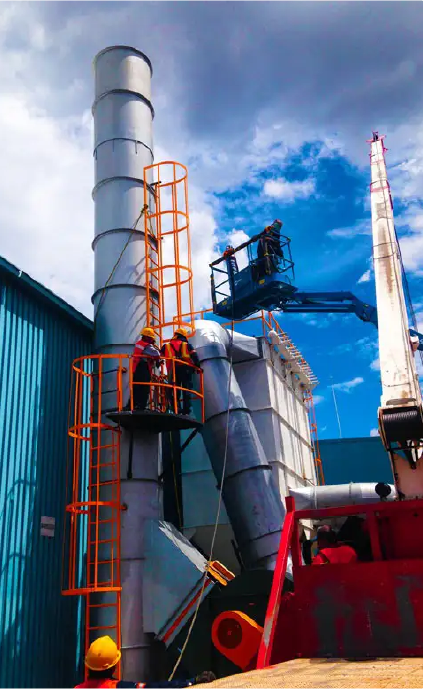 Instalación de colector de polvo industrial en planta manufacturera Técnicos instalando colector de polvo industrial con ductos verticales y chimenea metálica.